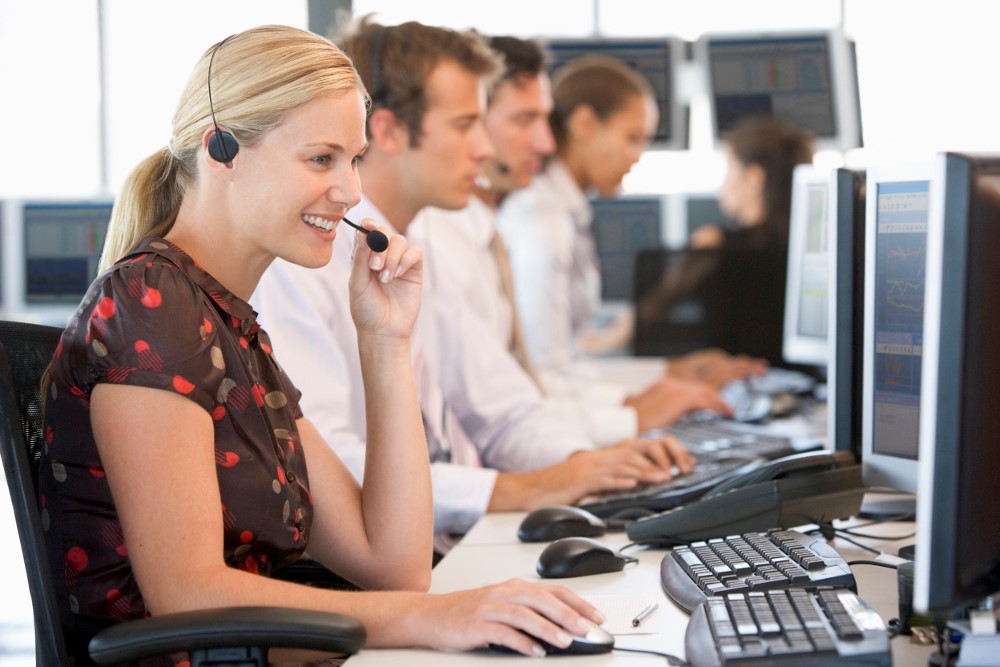 Four call center employees wearing headsets work at computers in a modern office, focusing on their tasks.