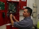 A technician inspects and adjusts wiring inside an open red electrical control panel mounted on a wall.