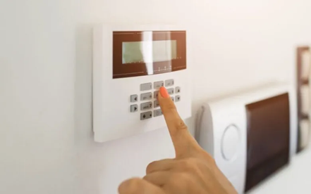 A person presses a button on a wall-mounted security system keypad.